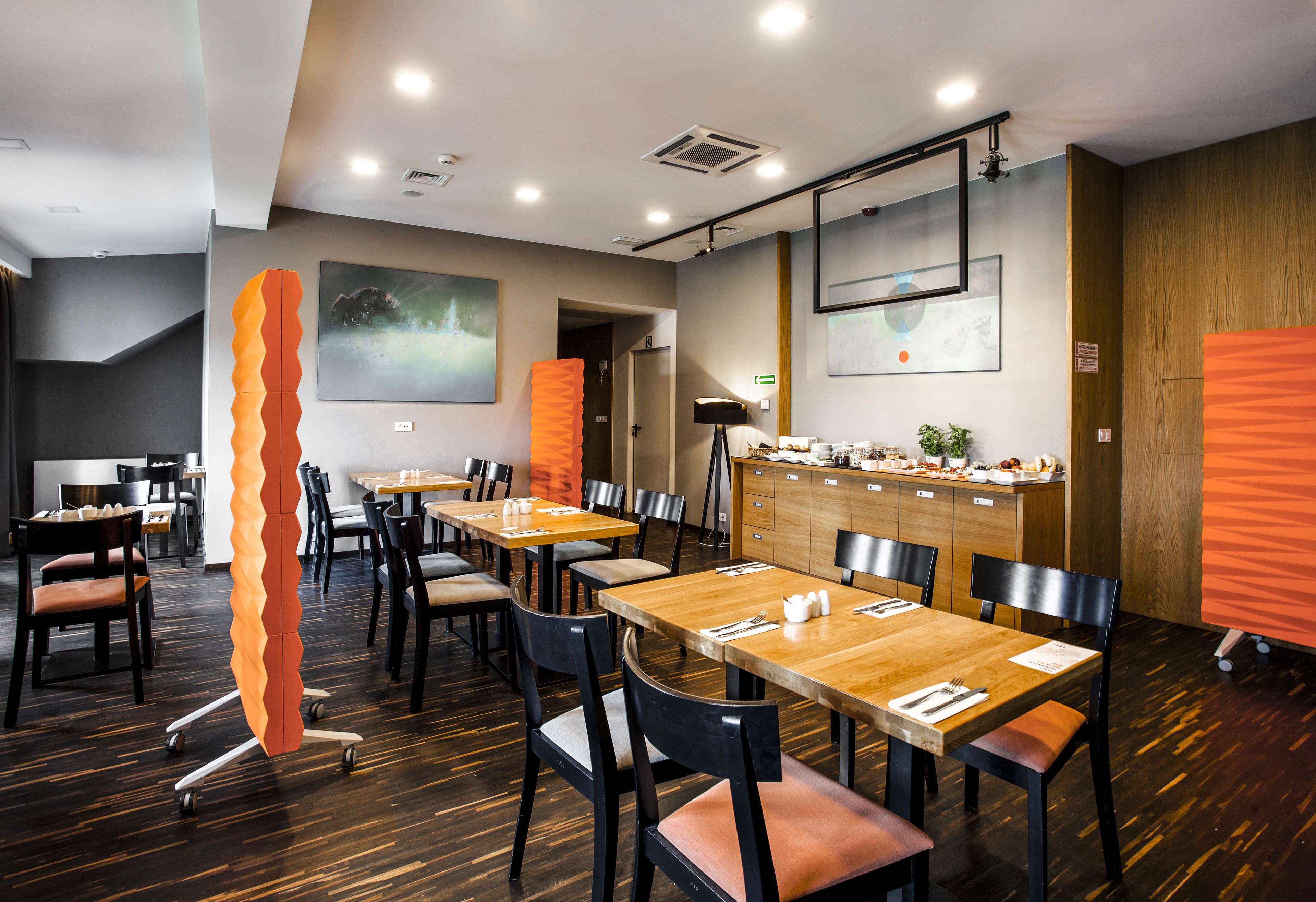 A modern dining area with wooden tables and chairs, a large abstract sculpture, and artwork on the walls.