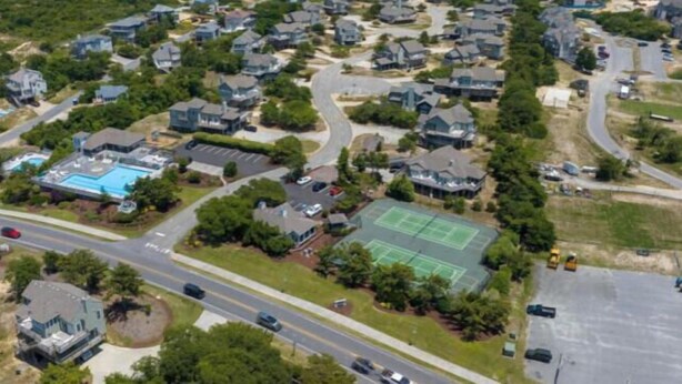 Ett flygbildsbild av ett bostadsområde med hus, vägar och en tennisbana.