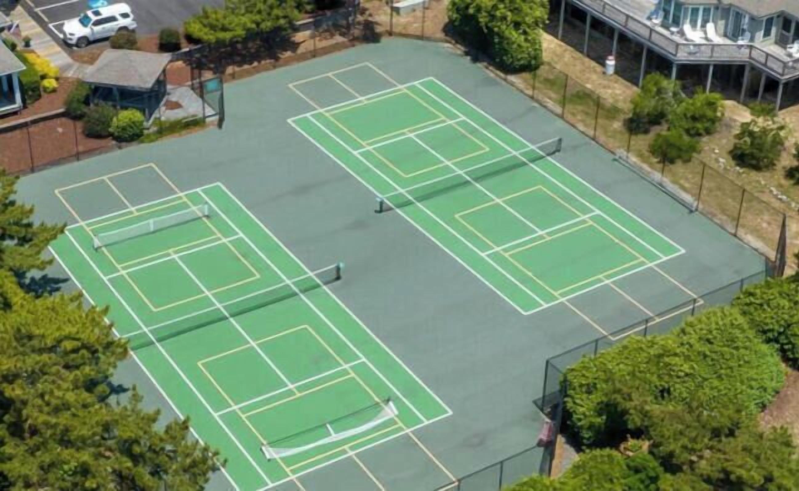 Vista aérea de un complejo de canchas de tenis con varias canchas, rodeado de árboles y edificios.