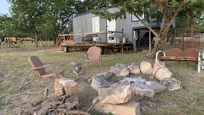 Ein rustikaler Außenbereich mit Feuerstelle, Holzmöbeln und einer kleinen Werkstatt.