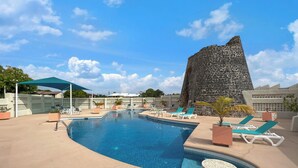 Un área de piscina con sillas de descanso y una gran formación rocosa al fondo.