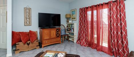 Una sala de estar con televisor, muebles de madera, ventilador de techo y cortinas rojas.