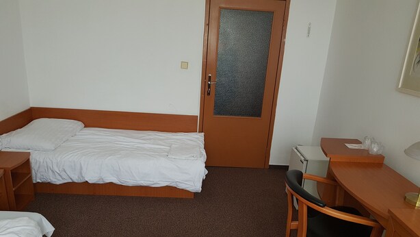 Habitació d'hotel amb dos llits individuals, una taula de nit de fusta, una cadira i una taula petita amb un comandament a sobre.