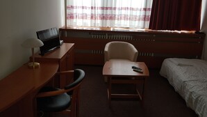 Habitació d'hotel amb escriptori, cadira, llit i finestra amb cortines.