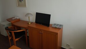Habitació d'hotel senzilla amb escriptori de fusta, televisió, làmpada i nevera petita.