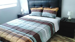 Un letto rifatto con una coperta a righe e due cuscini, un comodino con una lampada e un pavimento in legno decorato.