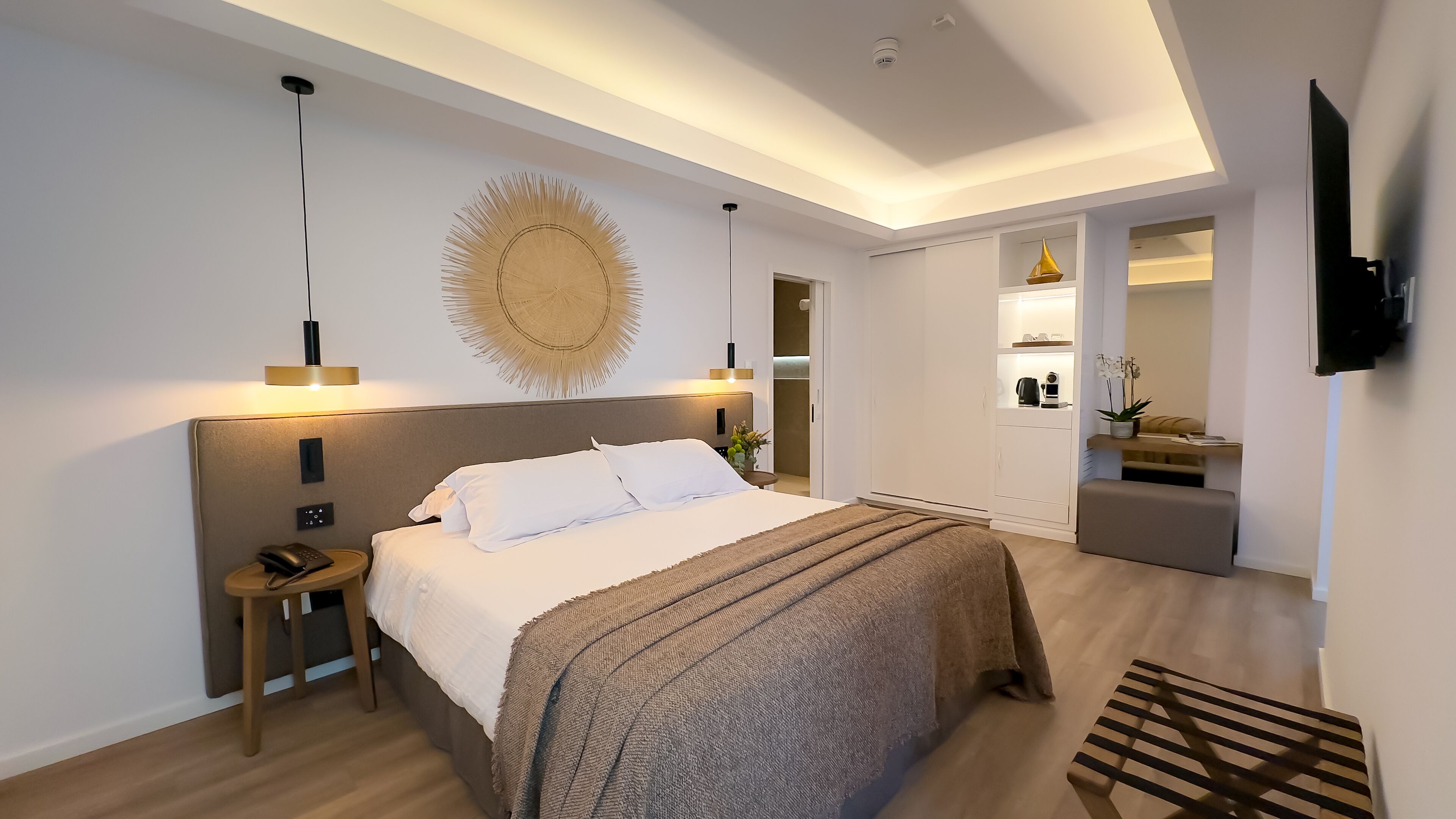 Une chambre d’hôtel moderne avec un grand lit, des tables de chevet, un téléviseur fixé au mur et un luminaire au plafond.