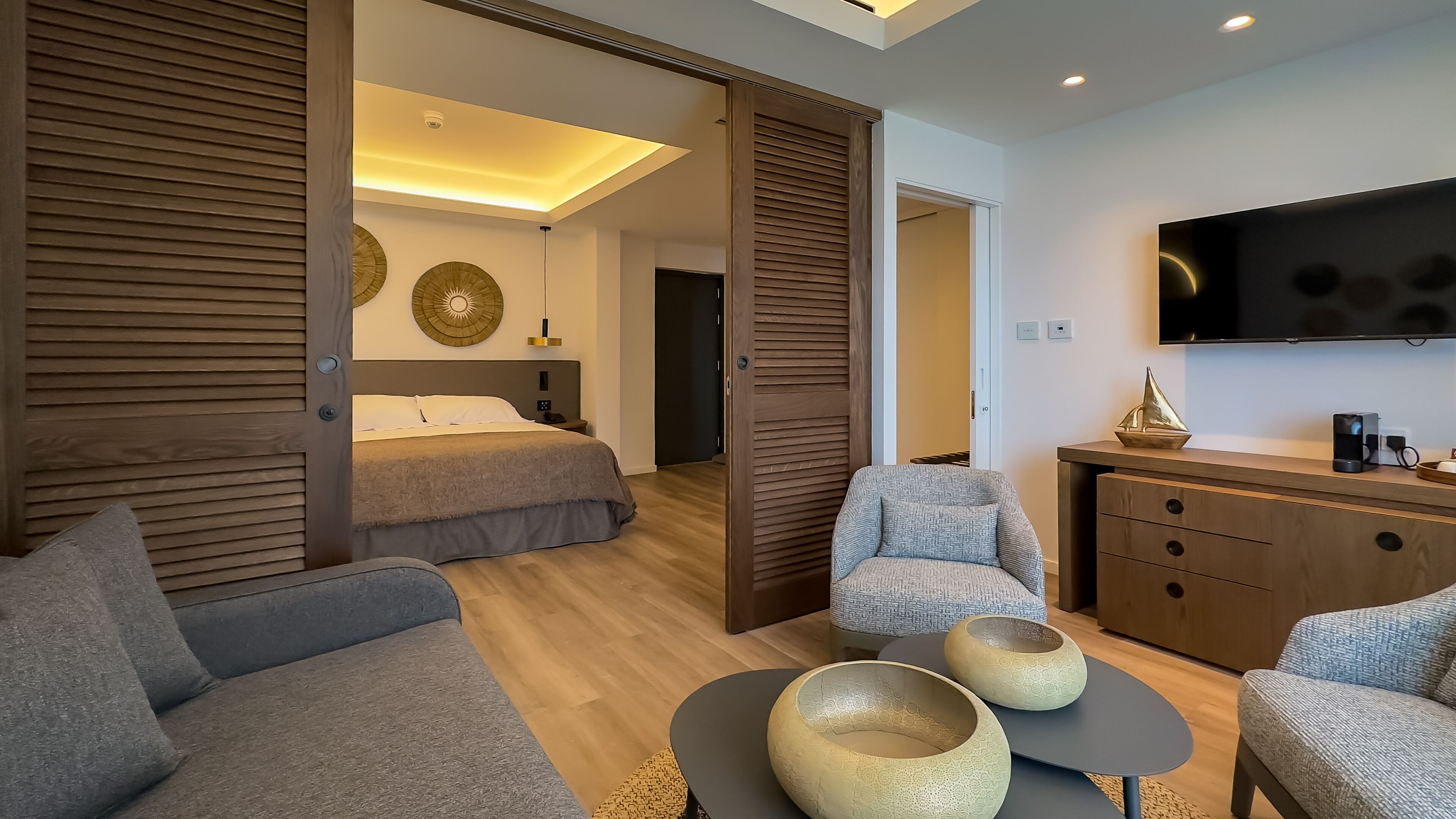 Quarto de hotel moderno com uma cama, um sofá, uma poltrona, uma mesa de centro e uma televisão.