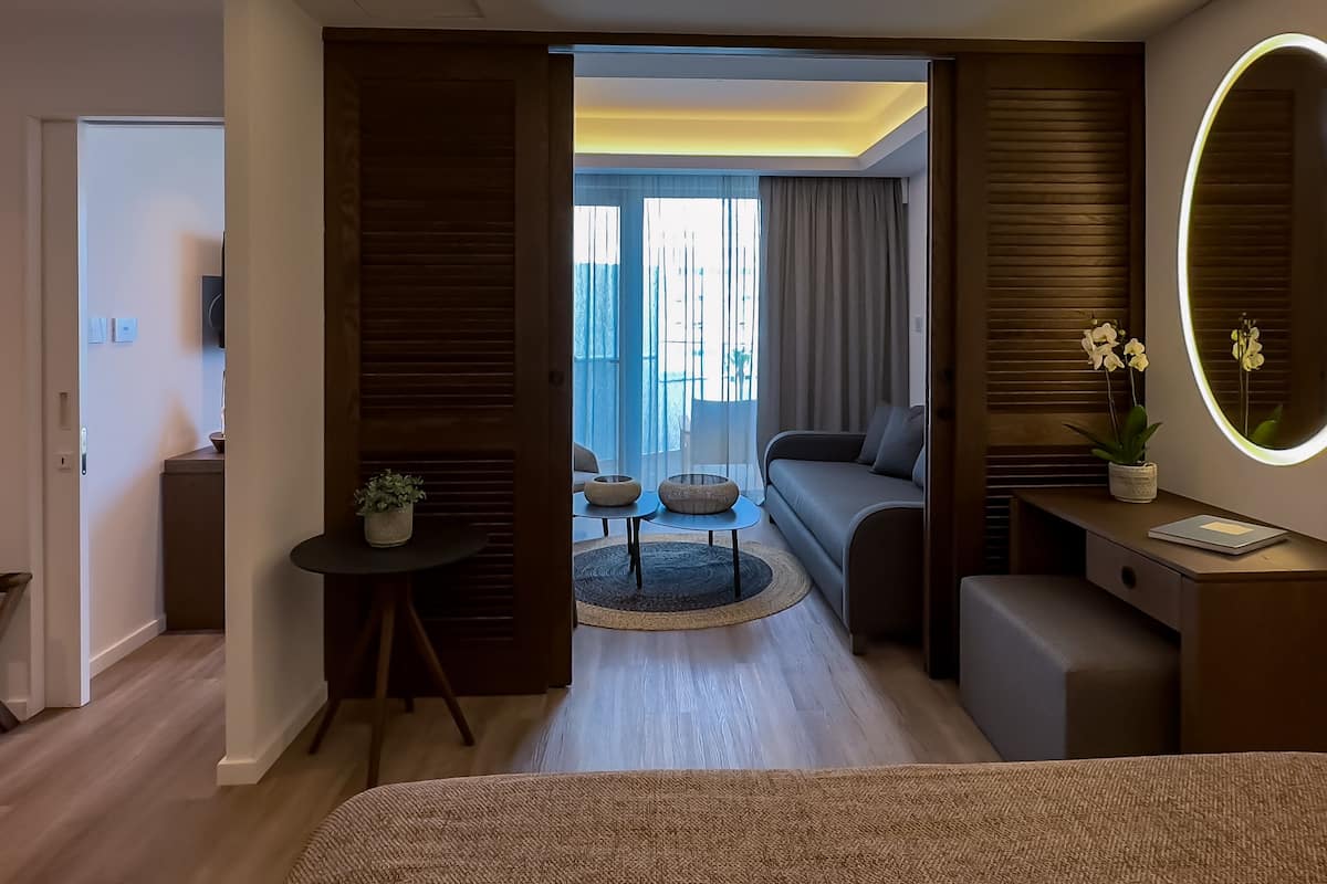 Une chambre d’hôtel moderne comprenant un lit, un bureau avec un miroir, une petite table avec une plante et un canapé.