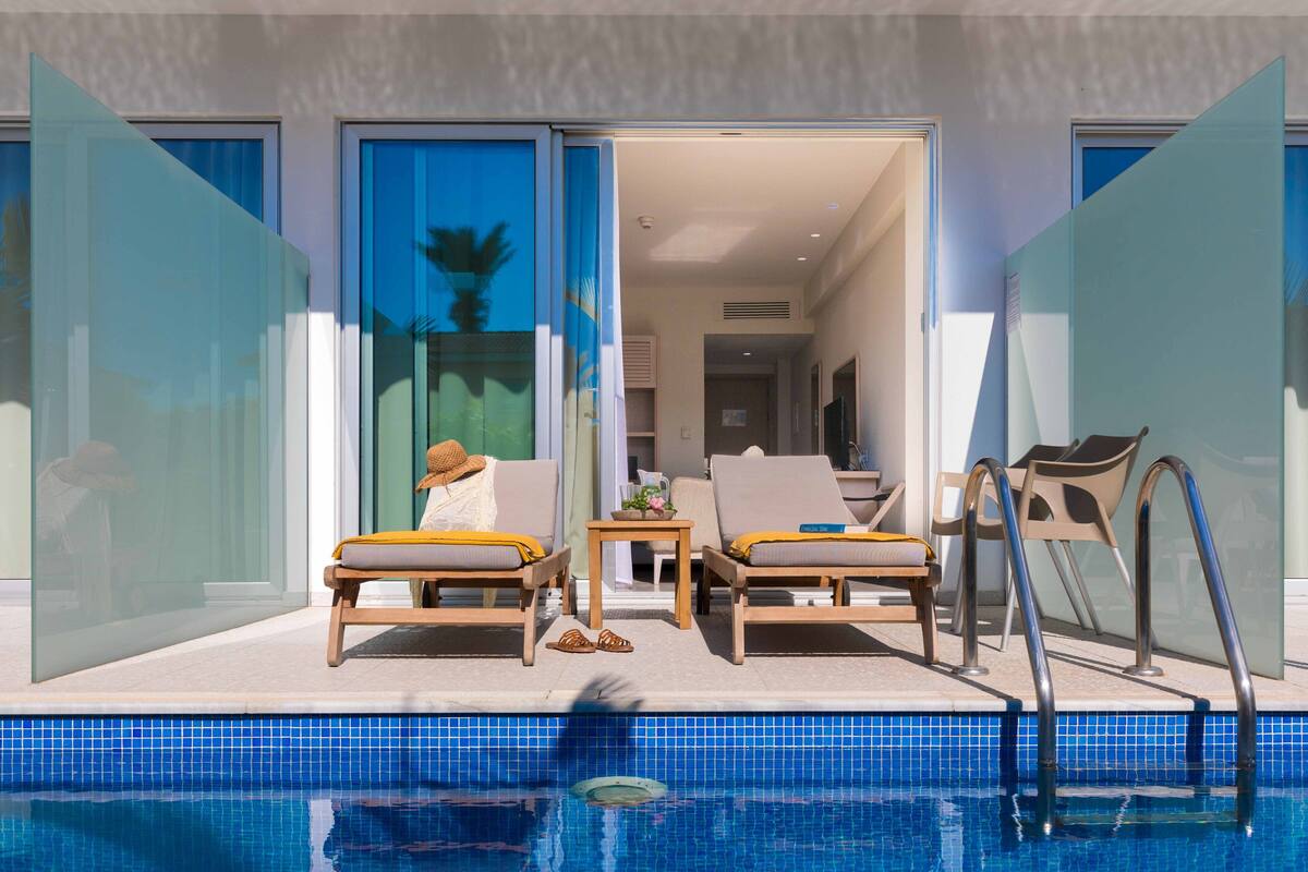 Un espace aménagé au bord de la piscine, avec des chaises longues, une piscine et une porte vitrée donnant accès à un espace intérieur.