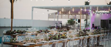 An outdoor dining area with clear chairs, wooden tables, and string lights.