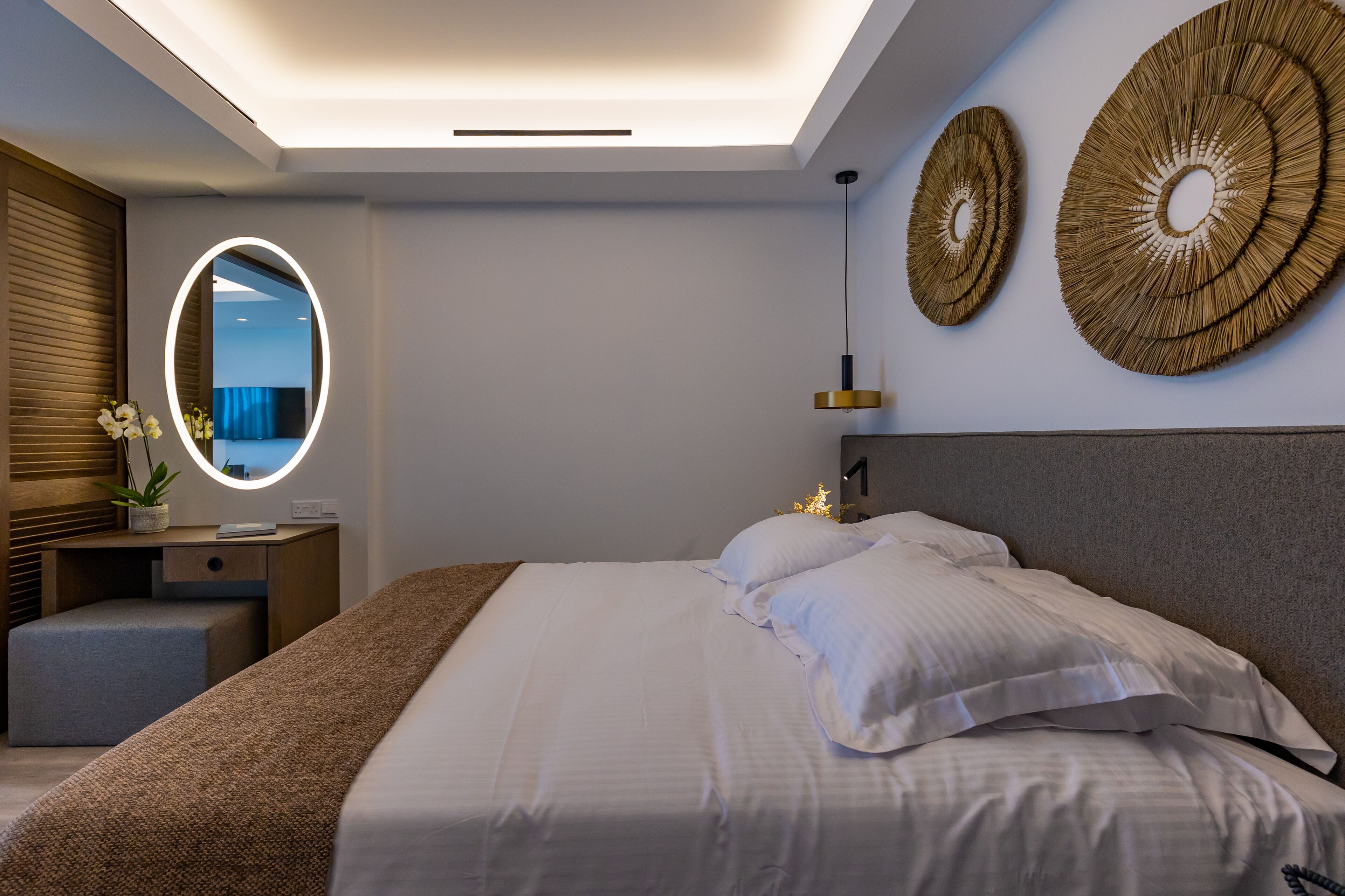 Un dormitorio moderno con una cama grande, una mesita de noche con lámpara, un espejo redondo y decoración en la pared.