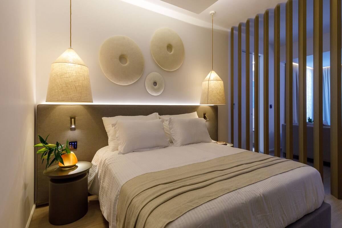 Une chambre moderne avec un grand lit, deux lampes fixées au mur et une table de chevet agrémentée d’une plante.