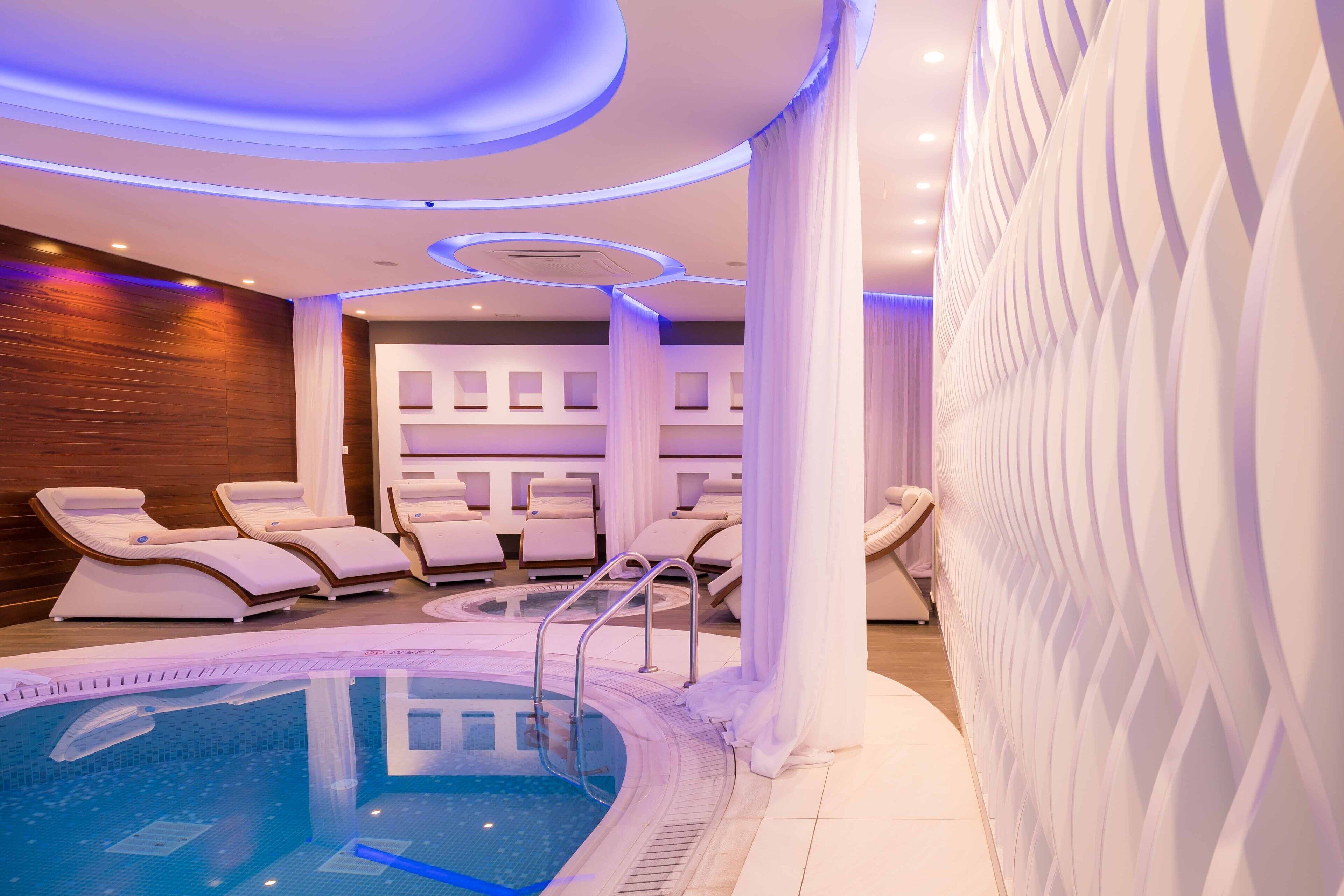 A modern spa area with a pool, lounge chairs, and a massage room.