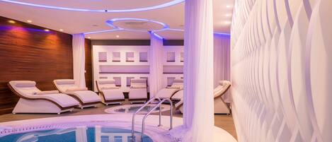 A modern spa area with a pool, lounge chairs, and a massage room.