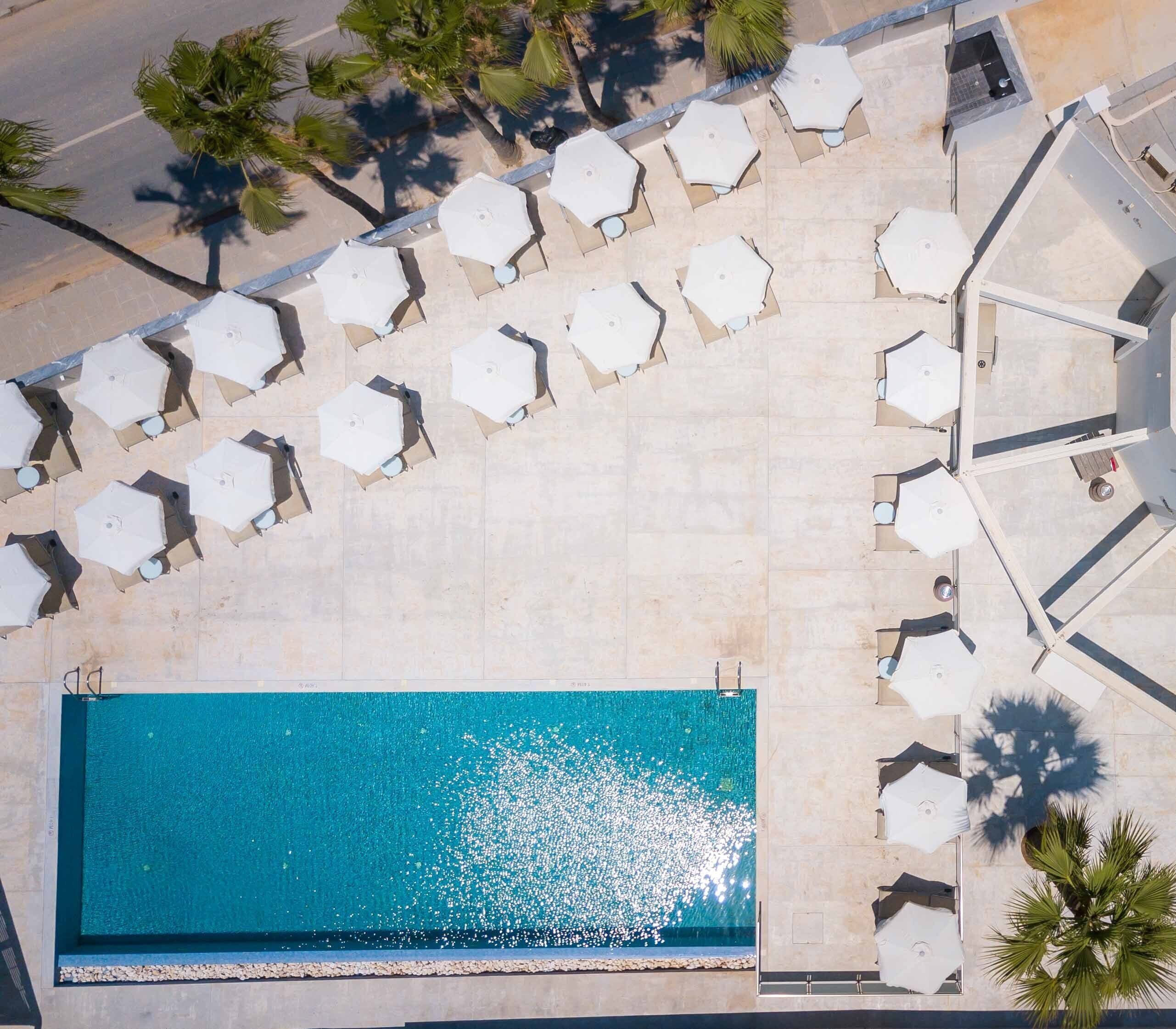 An aerial view of a swimming pool area with multiple sun loungers and palm trees.