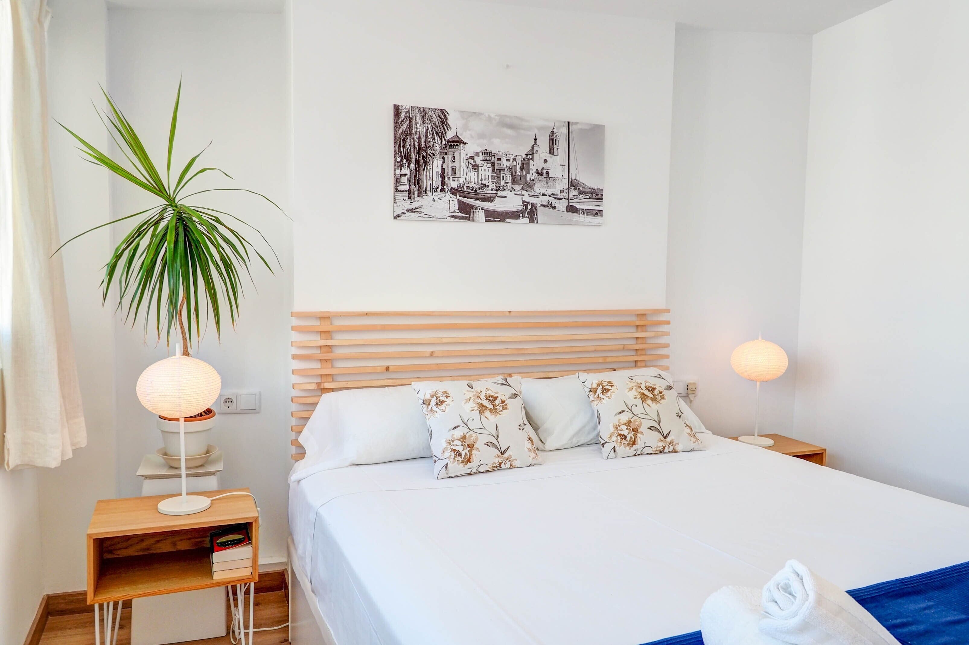 Ein ordentlich eingerichtetes Hotelzimmer mit Bett, Nachttisch, Lampe, Zimmerpflanze und einem Wandbild.