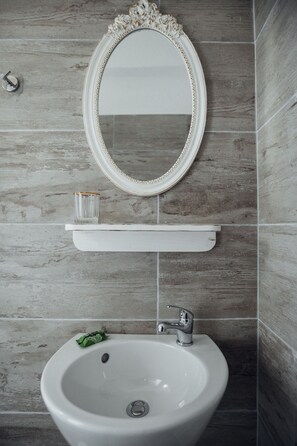 Ein Badezimmer mit einem weißen Waschbecken, einem Spiegel mit aufwendiger Rahmung und einem kleinen Glas auf dem Waschbecken.
