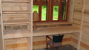 A wooden cabin interior with a desk, shelves, a chair, and a window with a view of greenery. - Réserve Naturelle de Boussière (Gigors-et-Lozeron)