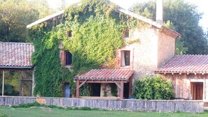 A rustic stone house with a red-tiled roof, partially covered in ivy, and a wooden porch. - Réserve Naturelle de Boussière (Gigors-et-Lozeron)