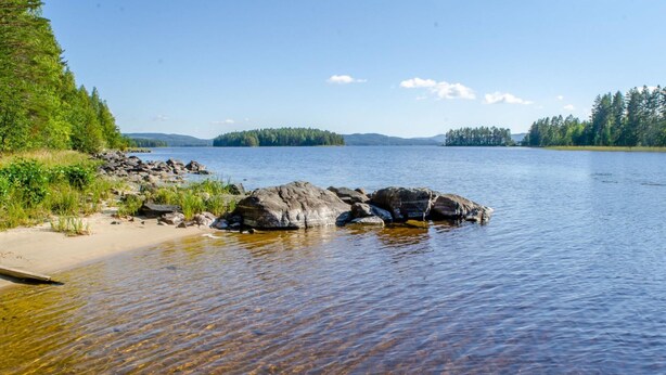 Un lac aux eaux claires, où l’on peut voir des rochers et une plage de sable.