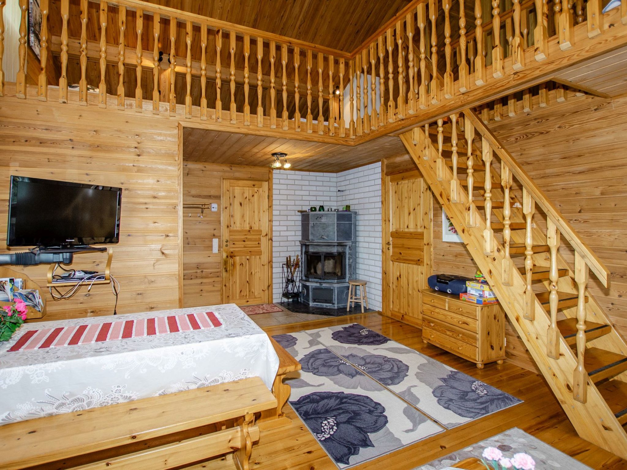 Een houten blokhut van binnen met een televisie, een open haard, een trap en een bed.