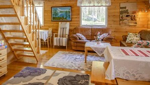 L’intérieur d’un chalet accueillant, avec un escalier en bois, un canapé en cuir marron, une table à manger et une grande fenêtre donnant sur la forêt.