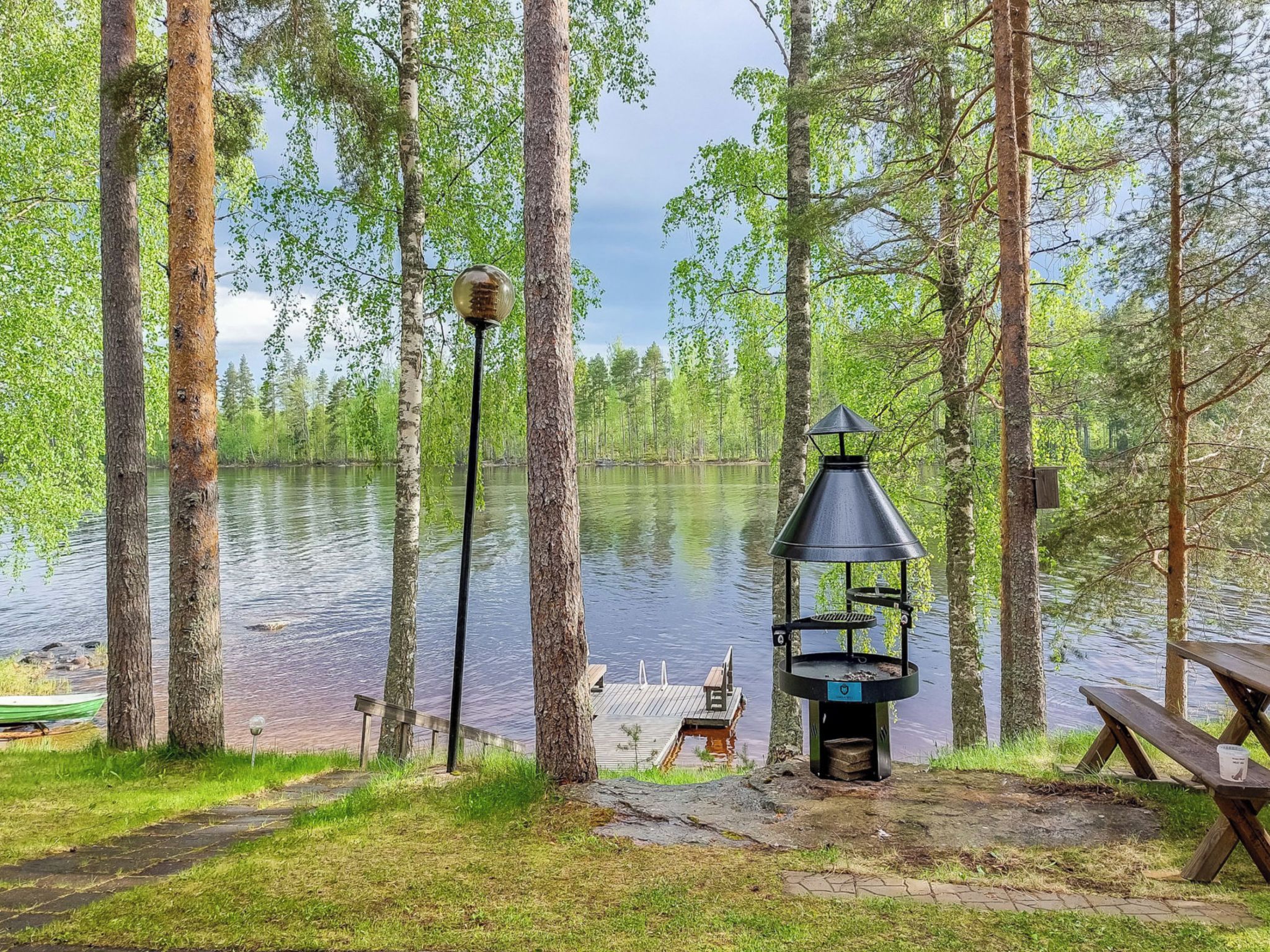 Leirintäalue järven rannalla, jossa on grilli, piknikpöytä ja valaisinpylväs.