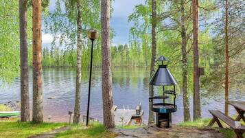 Leirintäalue järven rannalla, jossa on grilli, piknikpöytä ja valaisinpylväs.