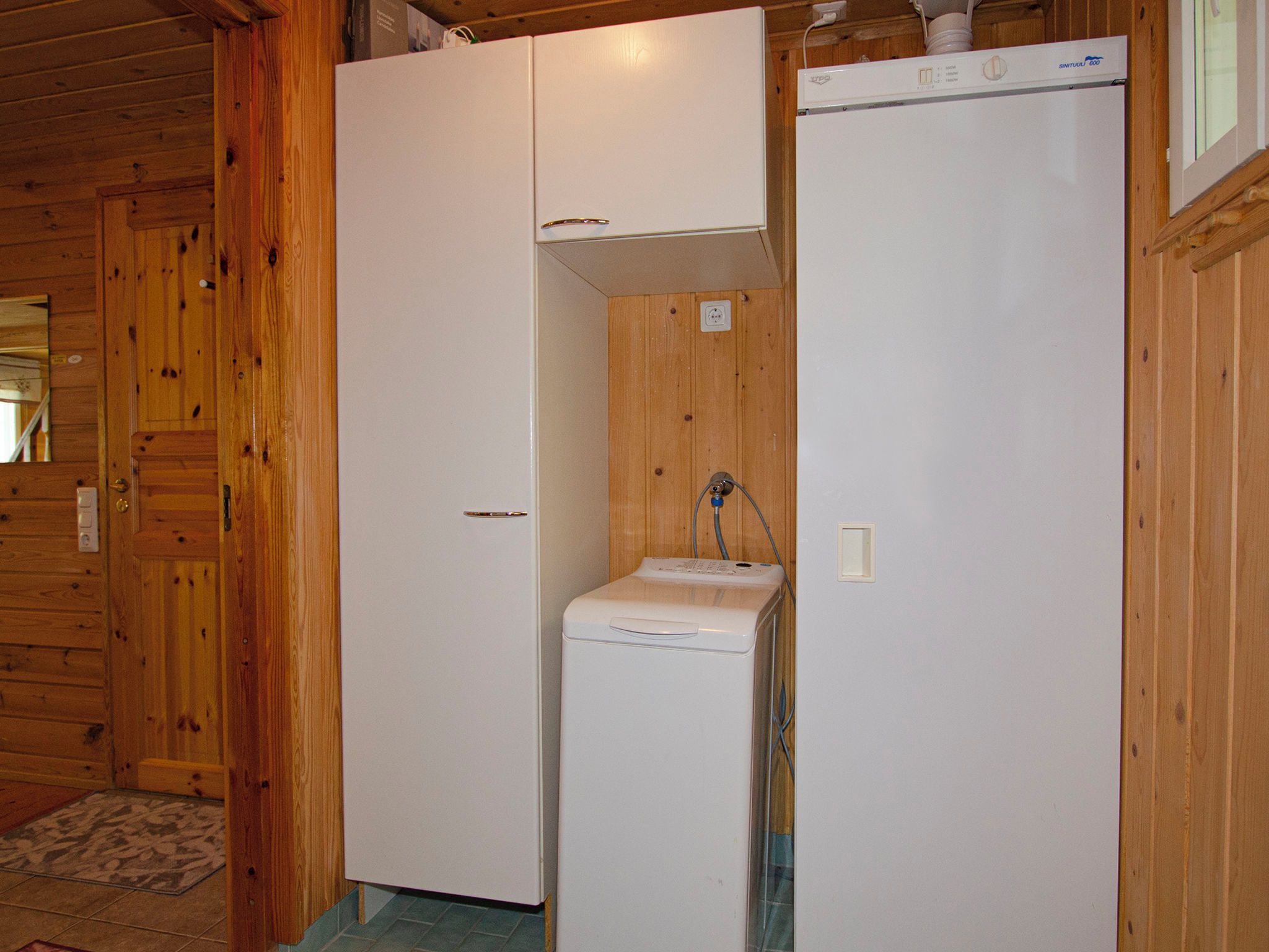 Een knus kamertje met houten wanden, een witte kast en een compacte wasmachine.