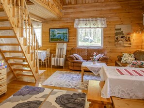 A cozy log cabin interior with a wooden staircase, a sofa, a dining table, and a painting on the wall.
