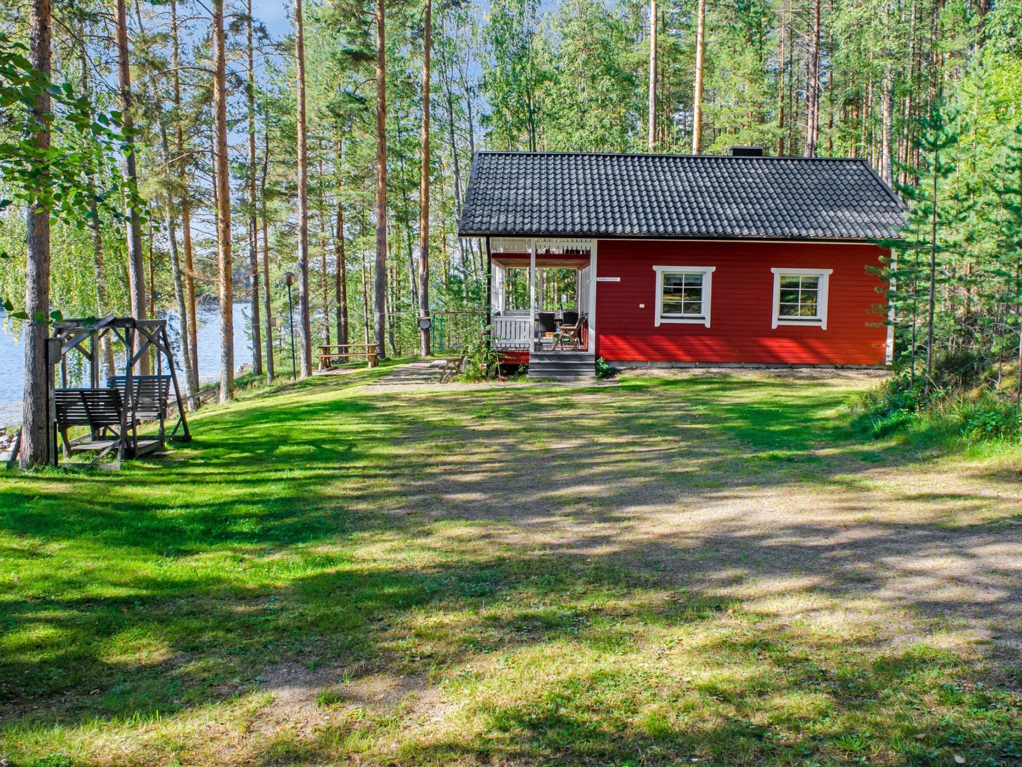 Punainen mökki, jossa on kuisti, ja sen ympärillä on metsää ja järvi.