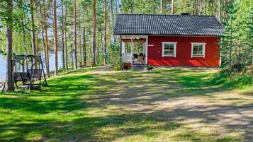 Punainen mökki, jossa on kuisti, ja sen ympärillä on metsää ja järvi.
