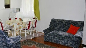 Um quarto com uma mesa de jantar, cadeiras, um sofá, uma televisão e uma janela com cortinas.