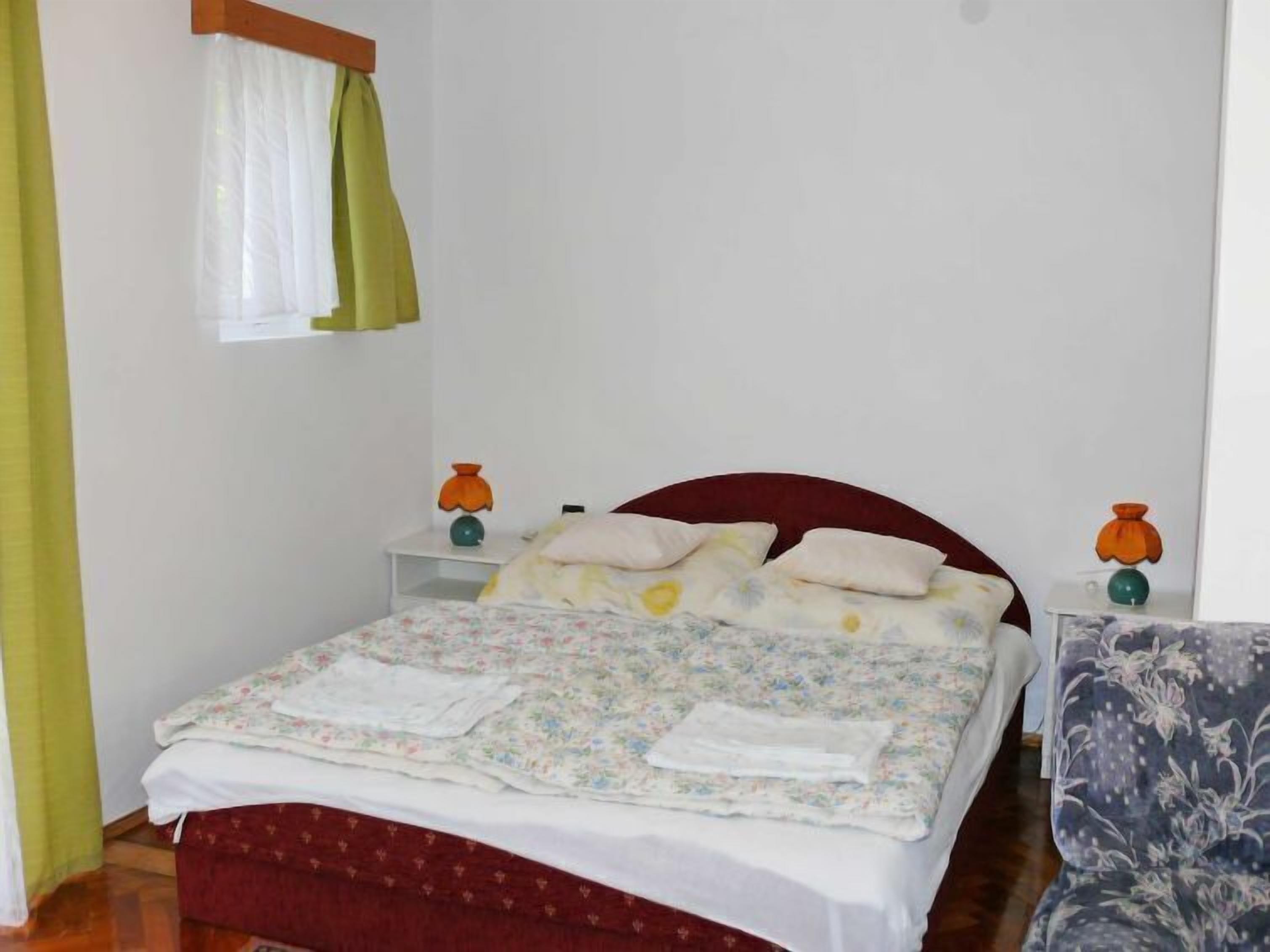 A bedroom with a bed, nightstands, a chair, and a window with curtains.