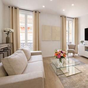 A modern living room with a beige sofa, a glass coffee table, and a vase of flowers.