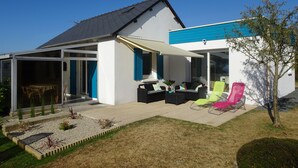 Une maison moderne dotée d’un patio couvert, d’un espace salon extérieur et d’un jardin.