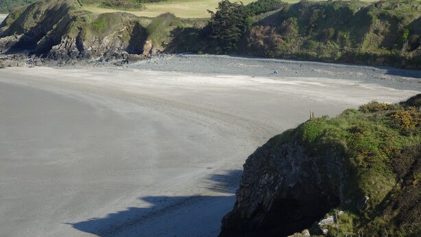Un paysage côtier caractérisé par une plage de sable, des falaises rocheuses et des collines verdoyantes.