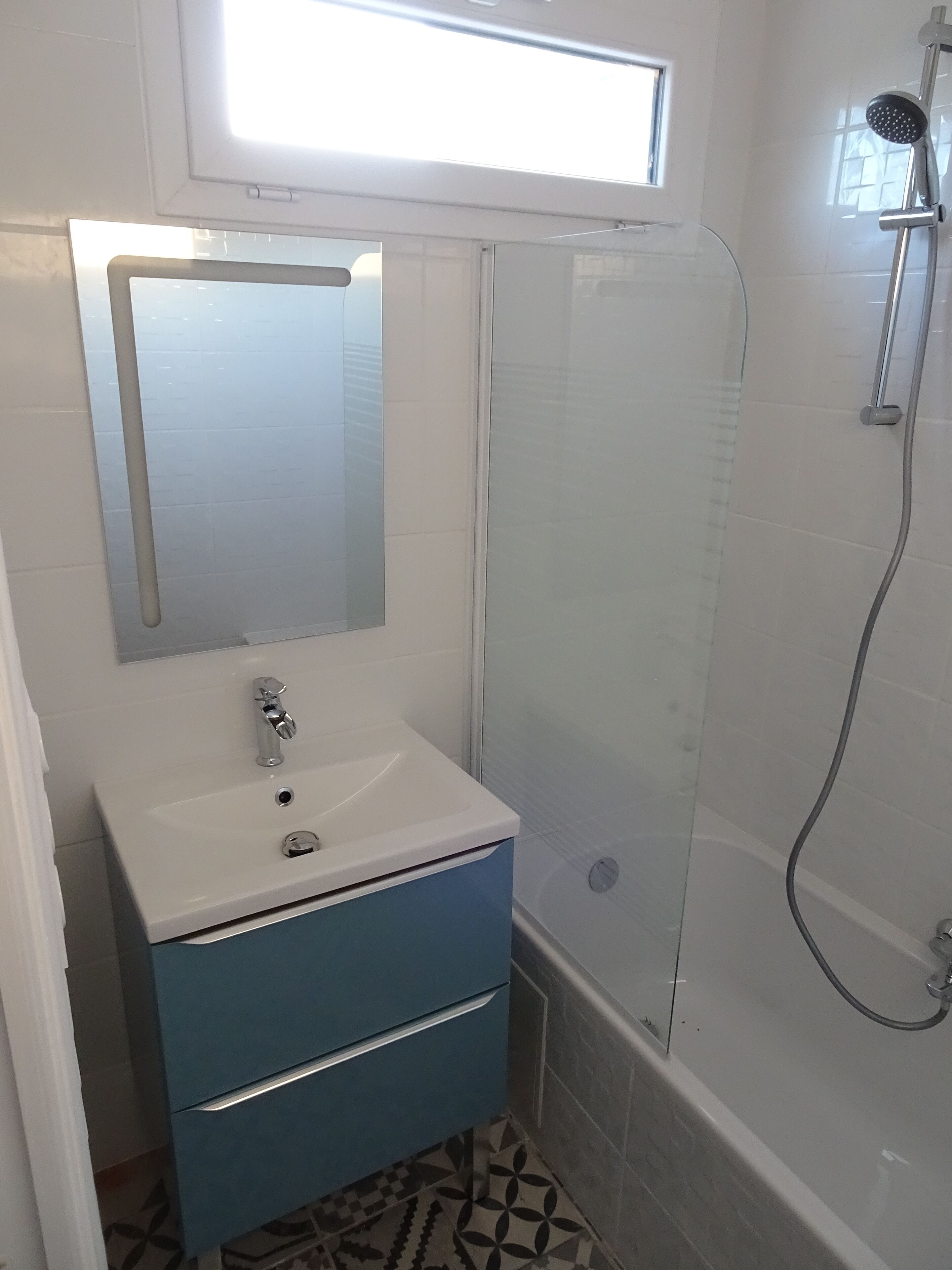 Une salle de bain avec un lavabo blanc, un meuble bleu et une douche en verre.