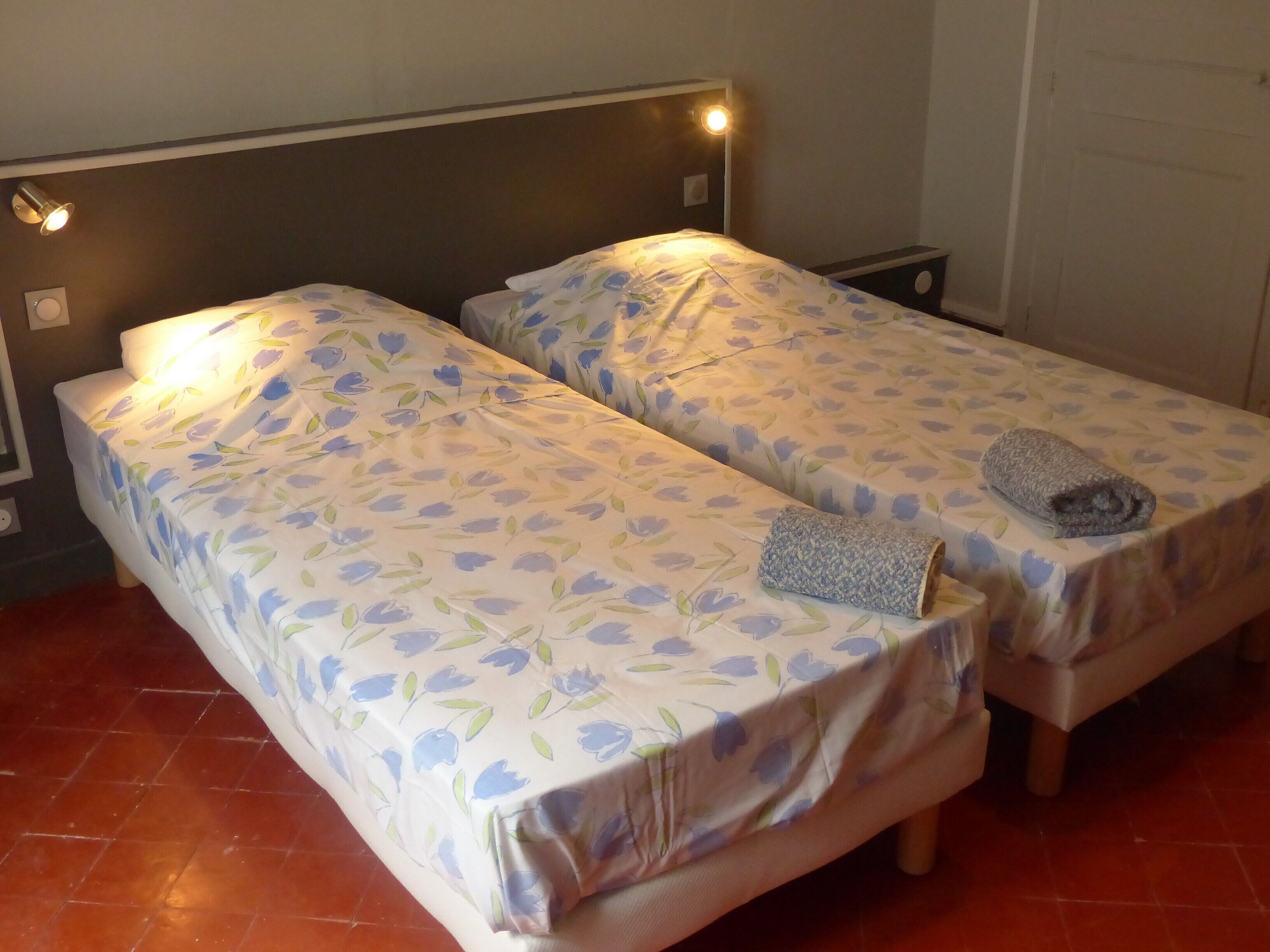 Habitació amb dos llits individuals, cadascun amb un llençol estampat de flors i una tovallola enrotllada sobre un dels llits.