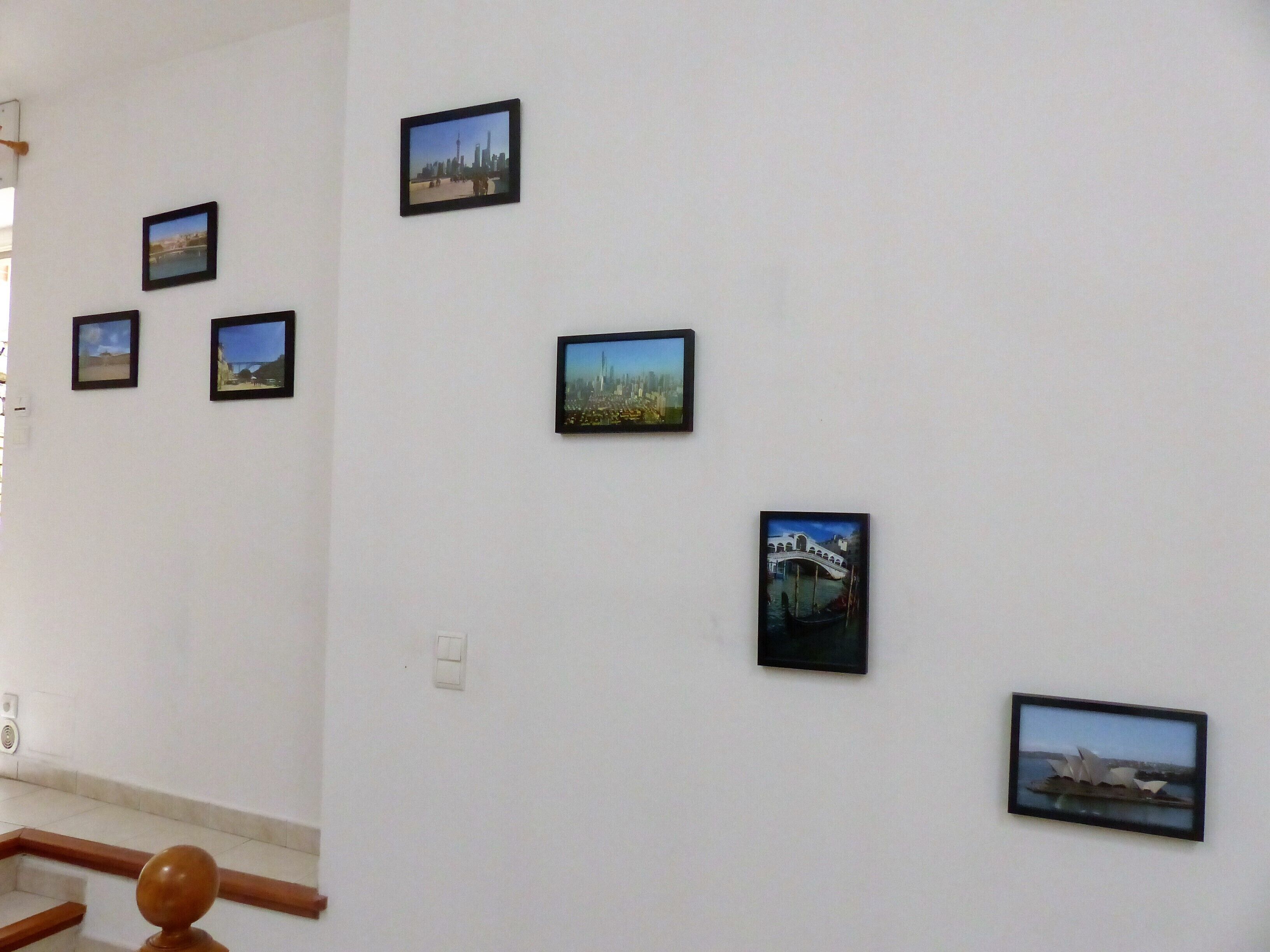 Een muur met meerdere ingelijste foto's van verschillende landschappen en stadsgezichten.