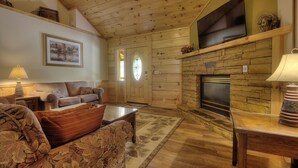 A cozy living room with wooden walls, a fireplace, a flat-screen TV, and a comfortable seating area. - Porch w/ swing & hot tub, sounds of stream, fireplace, pet & family friendly! (Pigeon Forge)