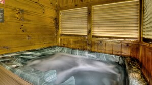 A wooden cabin with a hot tub, wooden walls, and a window with blinds. - Porch w/ swing & hot tub, sounds of stream, fireplace, pet & family friendly! (Pigeon Forge)