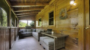 A wooden cabin with a covered porch, wicker furniture, and a laptop on a table. - Porch w/ swing & hot tub, sounds of stream, fireplace, pet & family friendly! (Pigeon Forge)