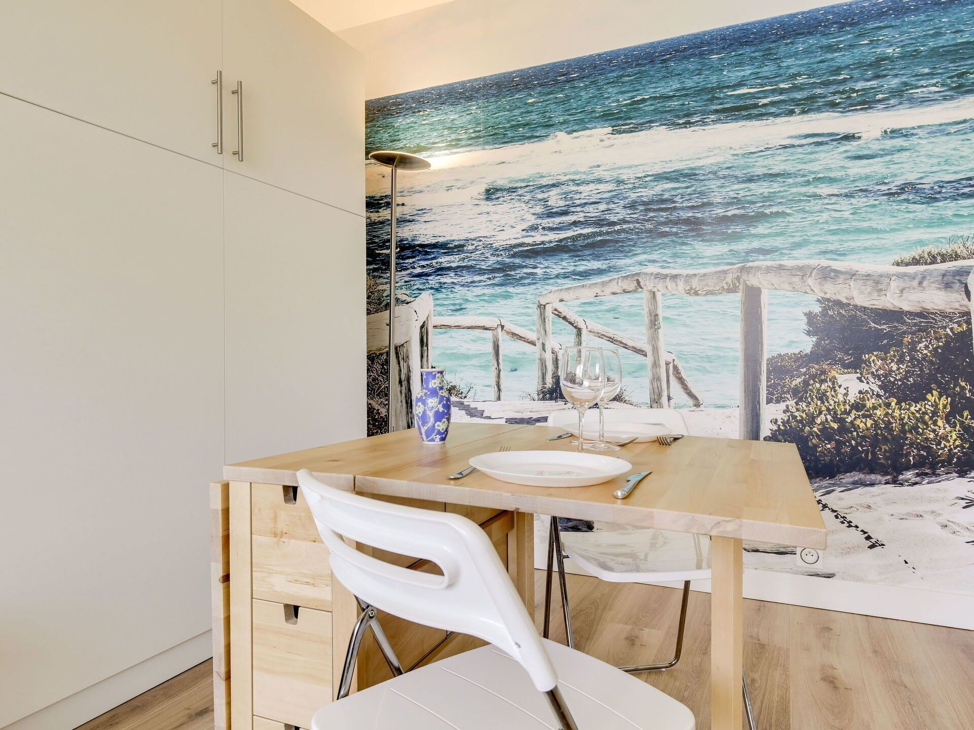 A dining area with a wooden table, white chairs, and a mural of a beach scene.