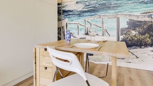 Ein Essbereich mit einem Holztisch, weißen Stühlen und einer Wandmalerei mit Strandmotiv.