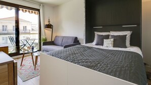 Ein modernes Schlafzimmer mit einem großen Bett, einem Sofa, einem kleinen Tisch und einem Balkon mit Blick auf Gebäude.