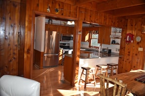 A wooden cabin interior with a kitchen, dining area, and a living room. - Secluded Cabin on a mountain stream on 7.5 acres (Lenoir)