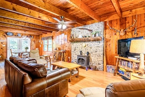 A cozy cabin interior with a stone fireplace, leather sofas, wooden floors, and a television. - Secluded Cabin on a mountain stream on 7.5 acres (Lenoir)