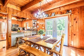 A wooden cabin interior with a dining table, benches, a chandelier, and a view of the outdoors. - Secluded Cabin on a mountain stream on 7.5 acres (Lenoir)